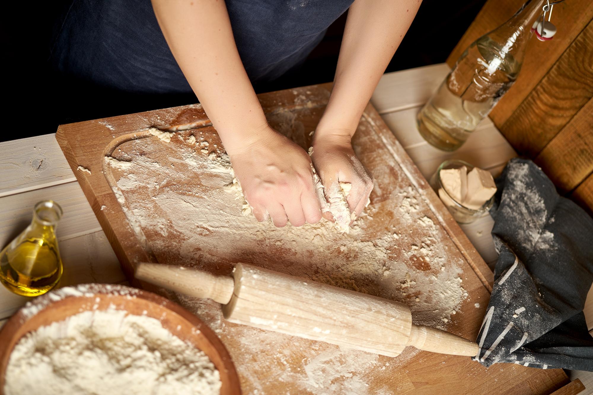 Hands kneading dough on wooden board